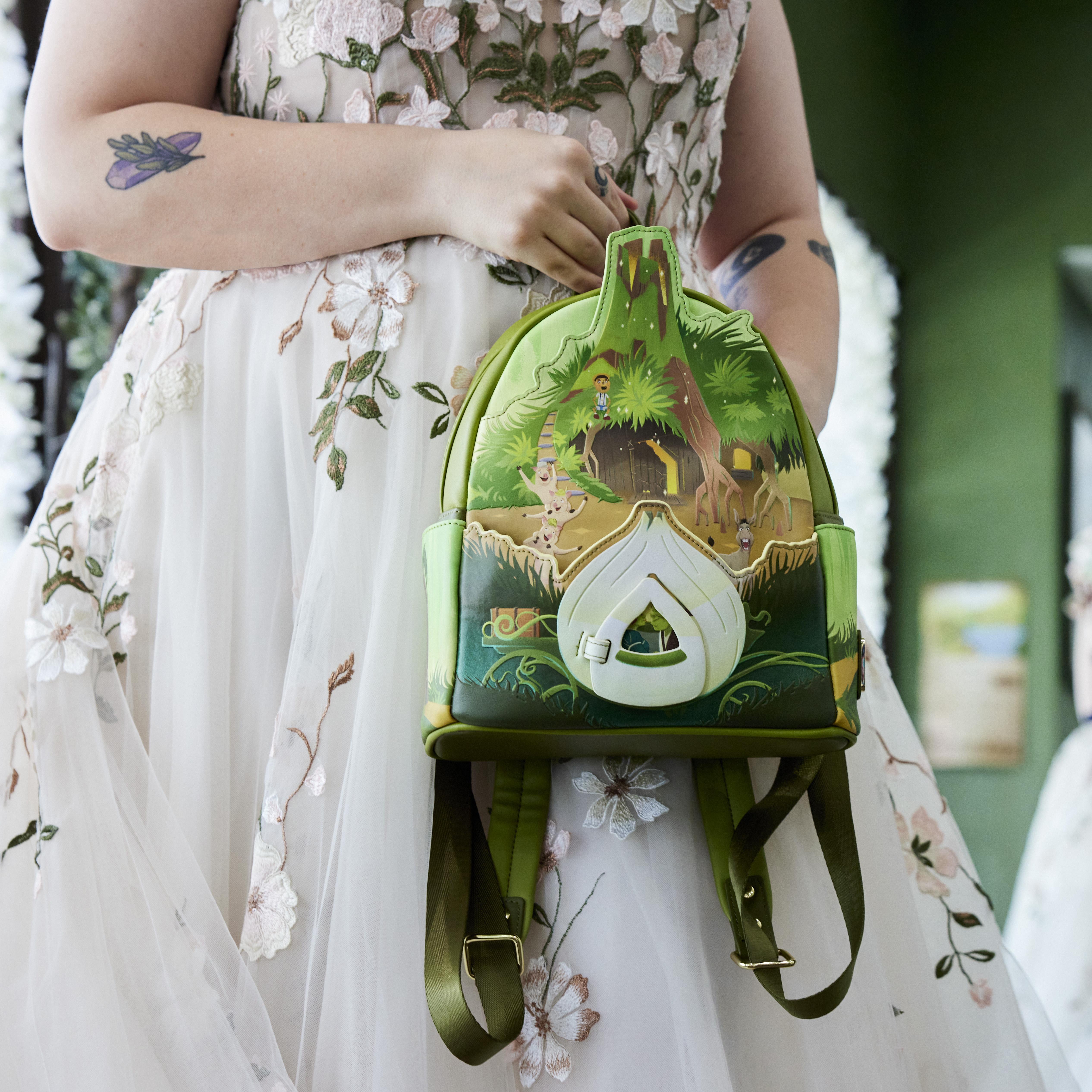 Close up of woman holding the Shrek Happily Ever After Mini Backpack against the skirt of a floral tulle wedding dress 